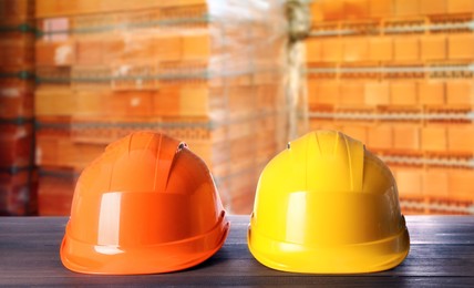 Hard hats on wooden surface near pallets with red bricks