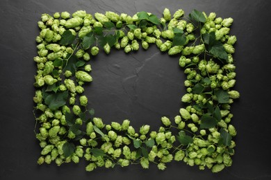 Frame of fresh green hops and leaves on black table, flat lay. Space for text