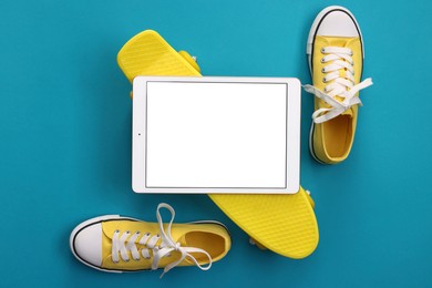 Photo of Modern tablet, skateboard and shoes on light blue background, flat lay. Space for text