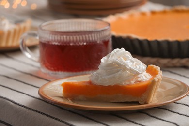 Piece of fresh homemade pumpkin pie served with whipped cream and tea on table