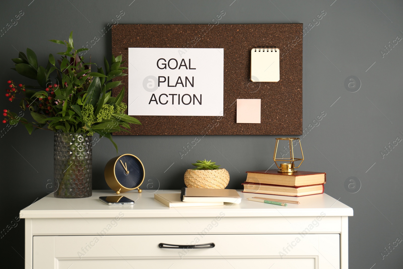 Photo of Paper with words Goal Plan Action pinned to cork board on grey wall indoors