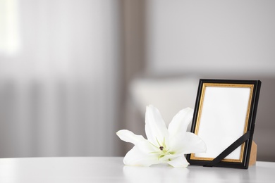 Funeral photo frame with black ribbon and lily on white table indoors. Space for design