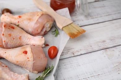 Photo of Raw marinated chicken drumsticks, rosemary and basting brush on white wooden table. Space for text