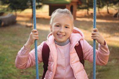 Photo of Cute little girl with backpack on swing outdoors