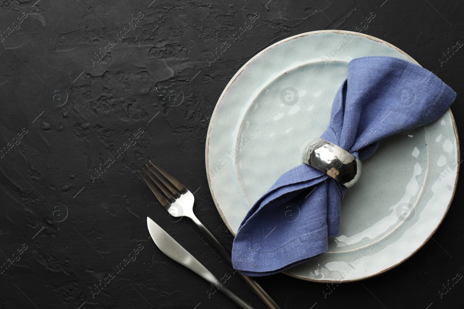 Photo of Stylish setting with cutlery, napkin and plate on dark textured table, flat lay. Space for text