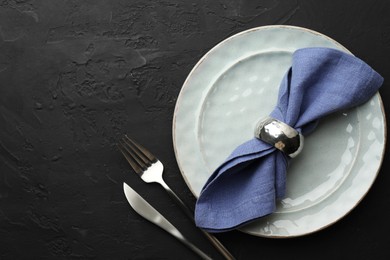 Photo of Stylish setting with cutlery, napkin and plate on dark textured table, flat lay. Space for text