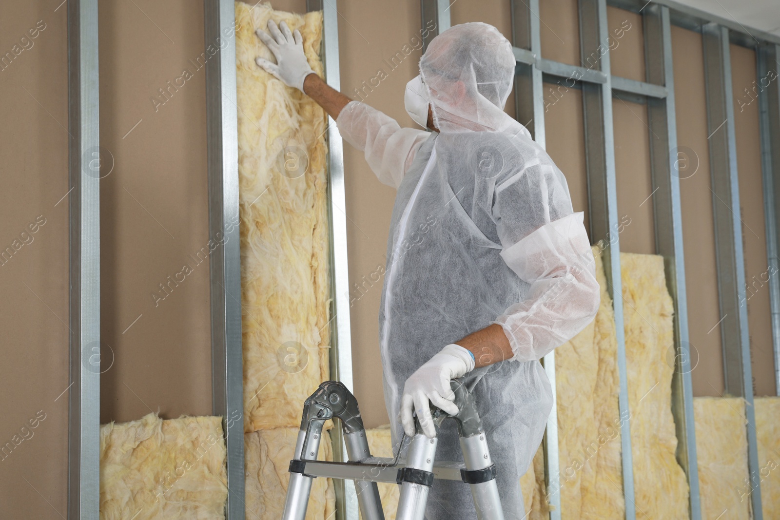 Photo of Worker in uniform insulating wall using ladder indoors