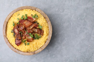 Photo of Cooked cornmeal with bacon and microgreens in bowl on light grey table, top view. Space for text