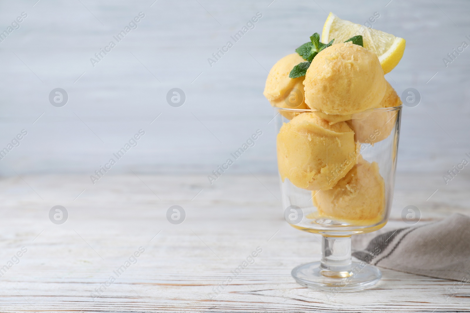 Photo of Yummy lemon ice cream in dessert bowl on white wooden table, space for text
