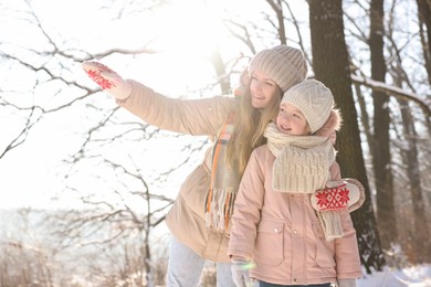 Photo of Family time. Mother showing something to her daughter in sunny snowy forest
