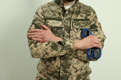 Man in military uniform with crossed arms and stethoscope on light background, closeup. Health care concept