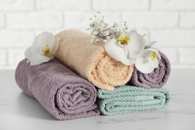 Photo of Rolled and folded towels with lilies on white table, closeup