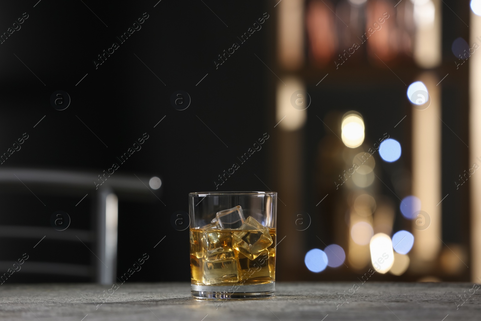 Photo of Golden whiskey with ice cubes on grey table indoors. Space for text