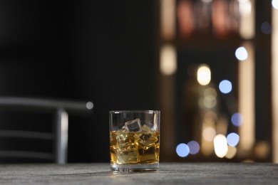 Golden whiskey with ice cubes on grey table indoors. Space for text