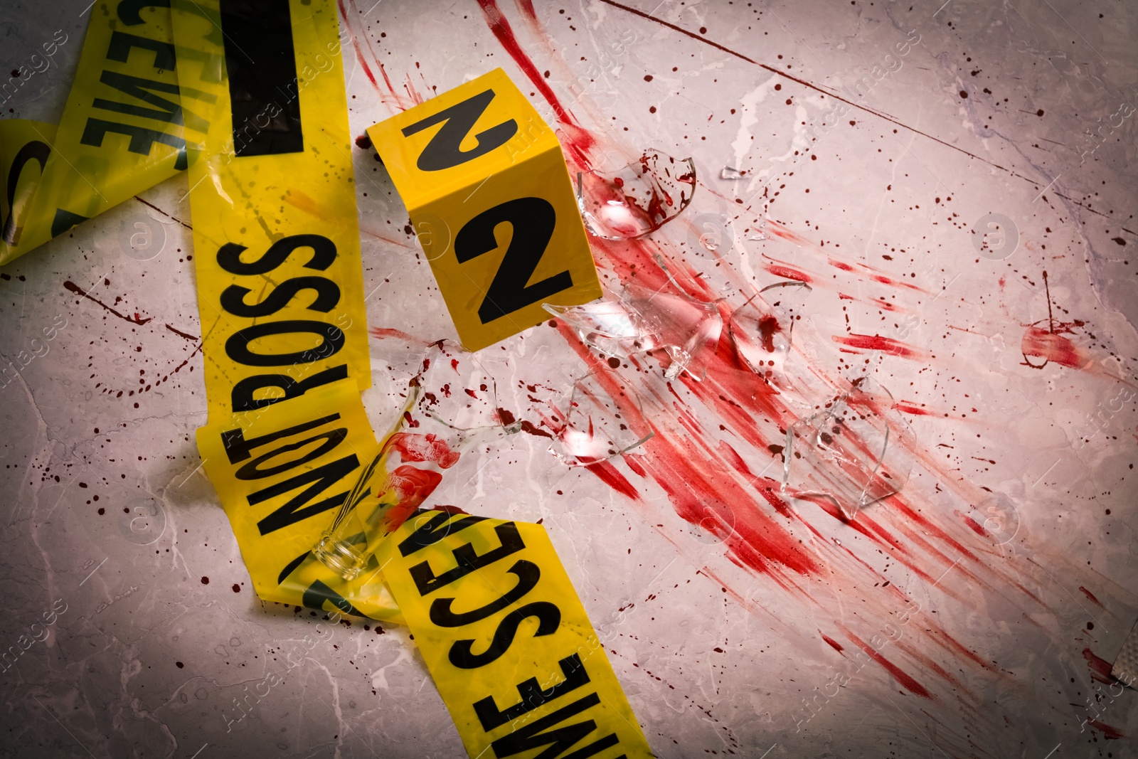 Photo of Yellow tape, crime scene marker and smithereens in blood on marble table, flat lay
