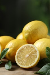 Photo of Fresh lemons and green leaves on wooden table, closeup