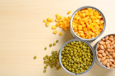 Photo of Open tin cans of conserved vegetables on wooden background, flat lay with space for text