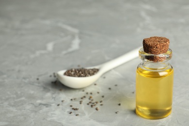 Photo of Bottle of oil and spoon with chia seeds on grey table. Space for text