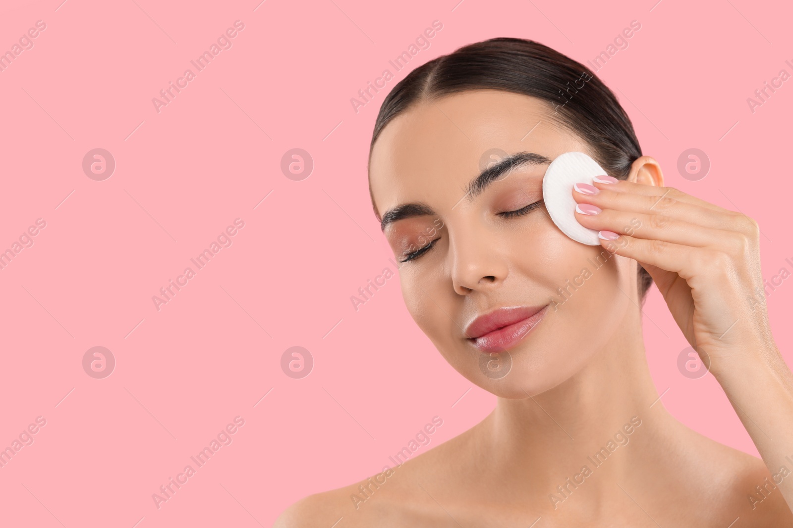 Photo of Beautiful woman removing makeup with cotton pad on pink background. Space for text