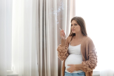 Photo of Young pregnant woman smoking cigarette at home. Harm to unborn baby
