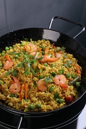 Photo of Tasty rice with shrimps and vegetables in frying pan on induction stove, closeup