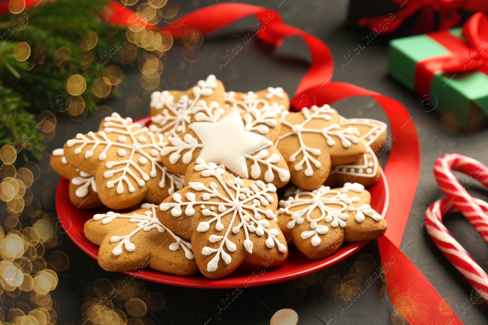 Photo of Tasty Christmas cookies with icing and red ribbon on black table