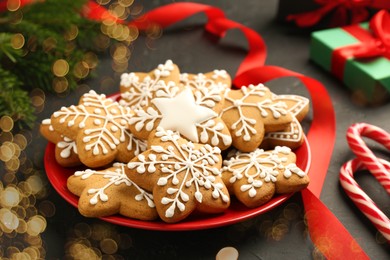 Tasty Christmas cookies with icing and red ribbon on black table