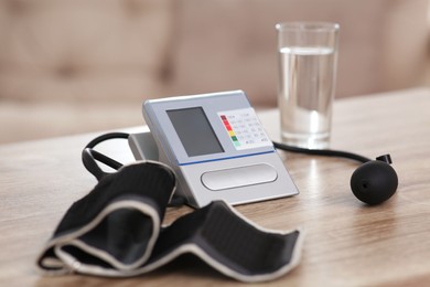 Photo of Modern blood pressure monitor and glass of water on wooden table indoors, closeup