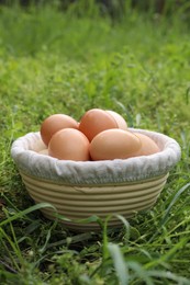 Photo of Fresh chicken eggs in basket on green grass outdoors