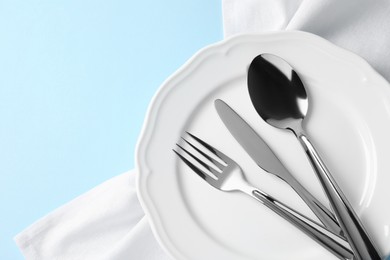 Stylish silver cutlery, plate and napkin on light blue background, top view. Space for text