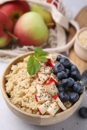 Photo of Bowl of delicious cooked quinoa with apples, blueberries and chia seeds on light grey table