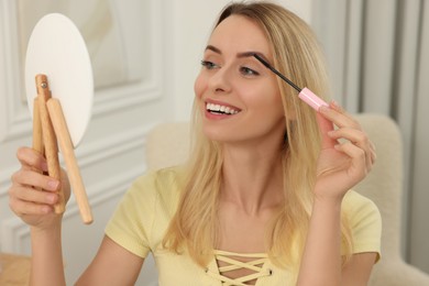 Photo of Beautiful woman with mirror applying mascara at home