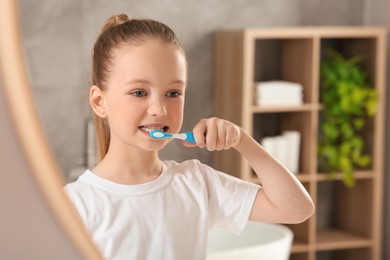 Photo of Cute little girl brushing her teeth with plastic toothbrush near mirror in bathroom