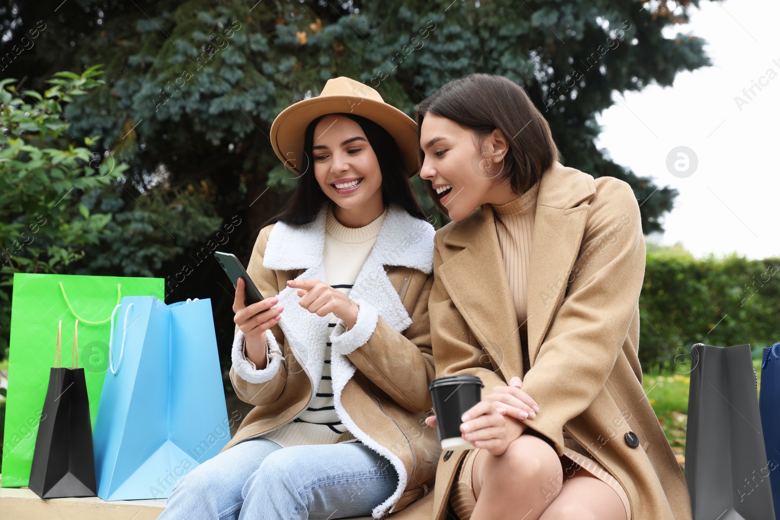 Photo of Special Promotion. Happy young women with smartphone and shopping bags in park