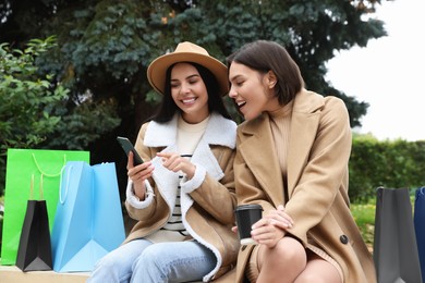 Special Promotion. Happy young women with smartphone and shopping bags in park