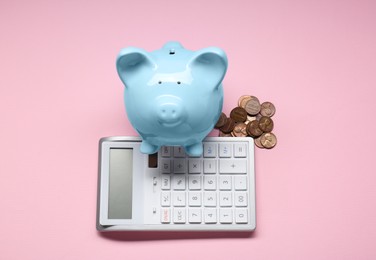 Calculator, coins and piggy bank on pink background, flat lay
