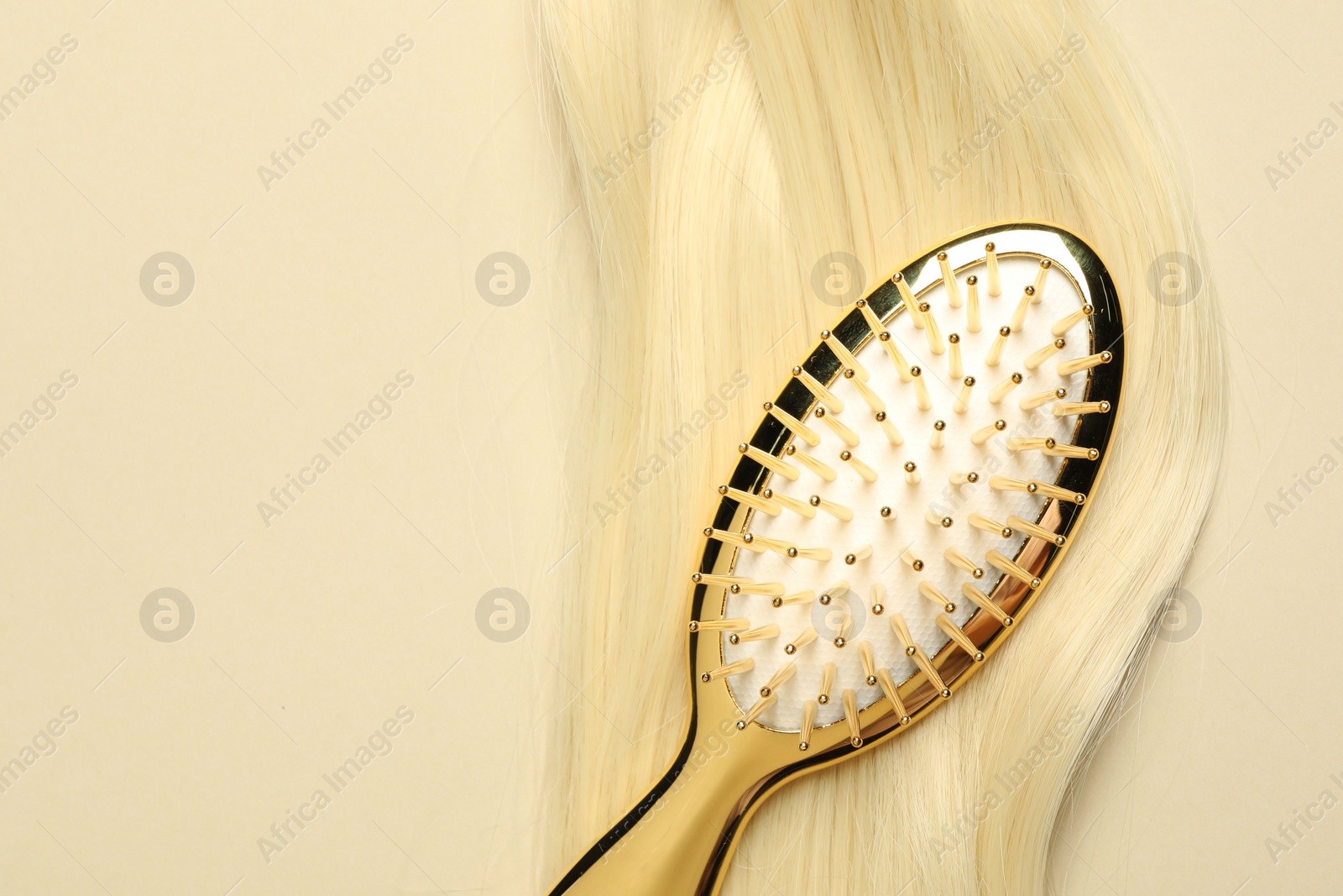 Photo of Stylish brush with blonde hair strand on beige background, top view. Space for text