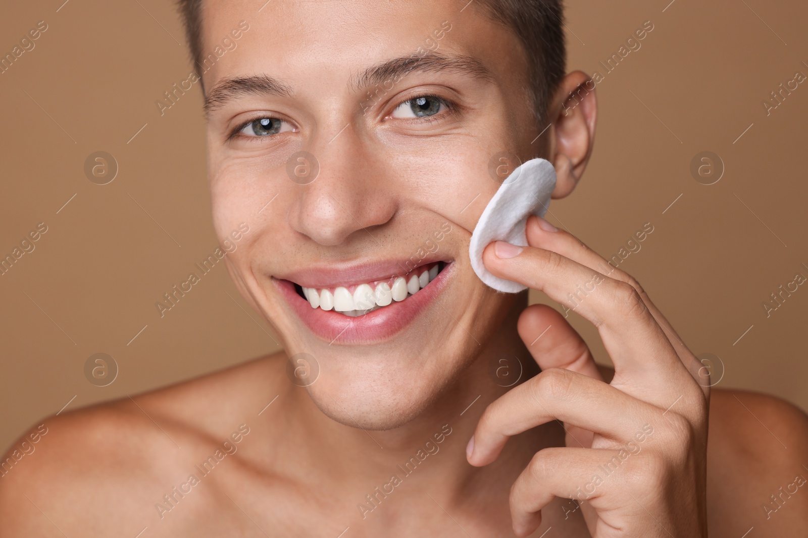 Photo of Handsome man cleaning face with cotton pad on beige background, closeup