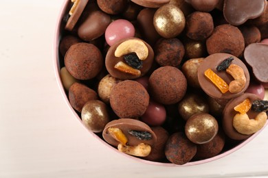 Photo of Different delicious chocolate candies in box on white wooden table, closeup