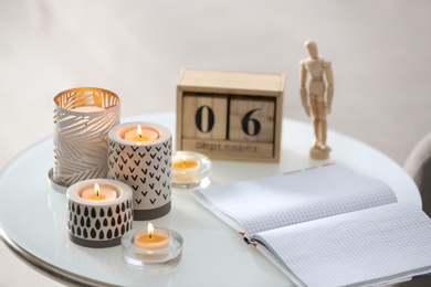Burning candles in holders and notebook on white table indoors