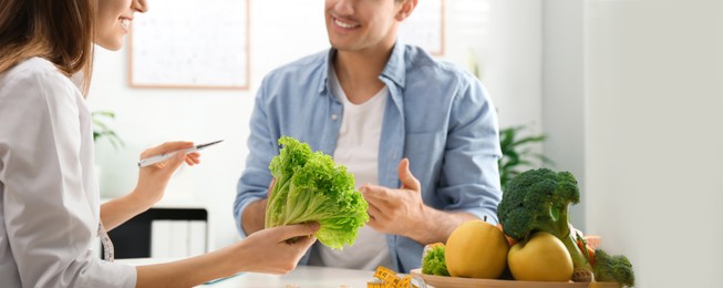 Young nutritionist consulting patient at table in clinic, closeup. Banner design