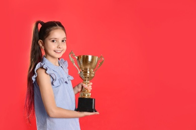 Photo of Happy girl with golden winning cup on red background. Space for text