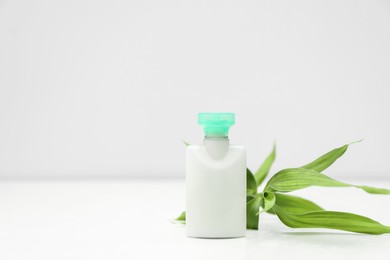 Photo of Mini bottlecosmetic product and green branch on light background. Space for text