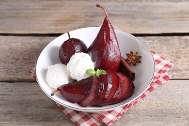 Tasty red wine poached pears and ice cream in bowl on wooden table, closeup