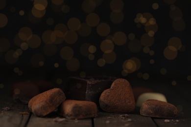 Photo of Delicious heart shaped chocolate candies on wooden table against blurred lights