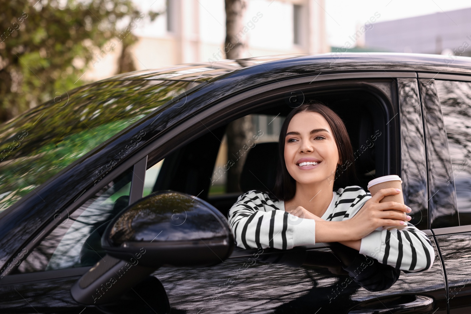 Photo of Young woman with cup of coffee sitting inside her modern car