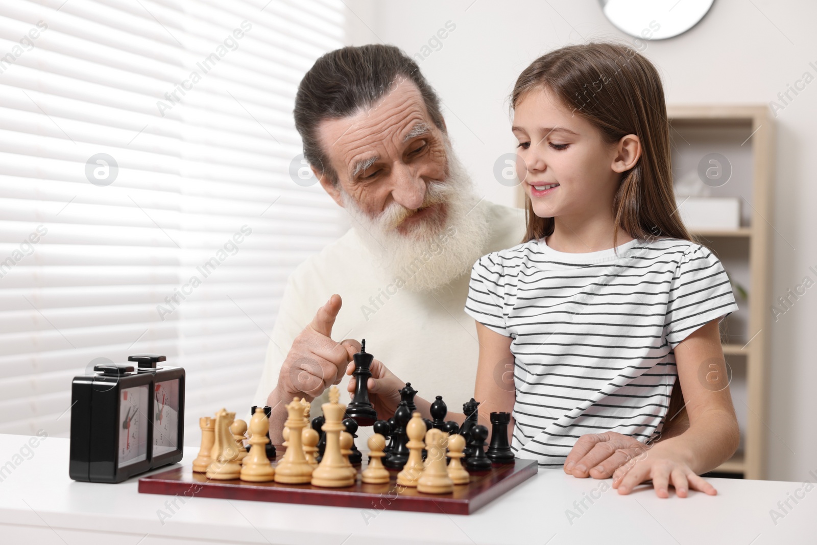 Photo of Senior man teaching his granddaughter to play chess at home