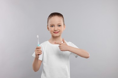 Photo of Happy girl holding electric toothbrush on light grey background