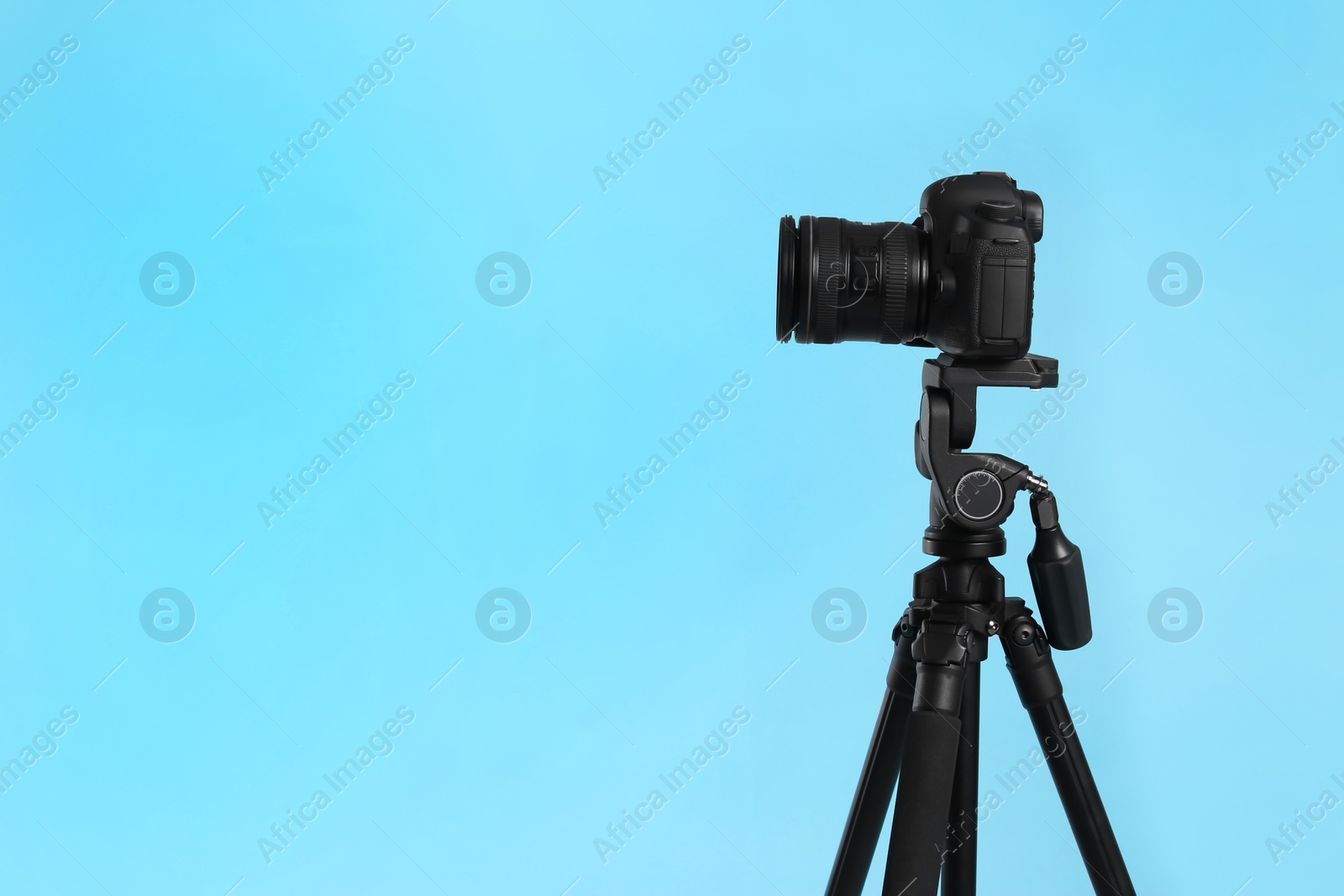 Photo of Modern tripod with professional camera on light blue background. Space for text