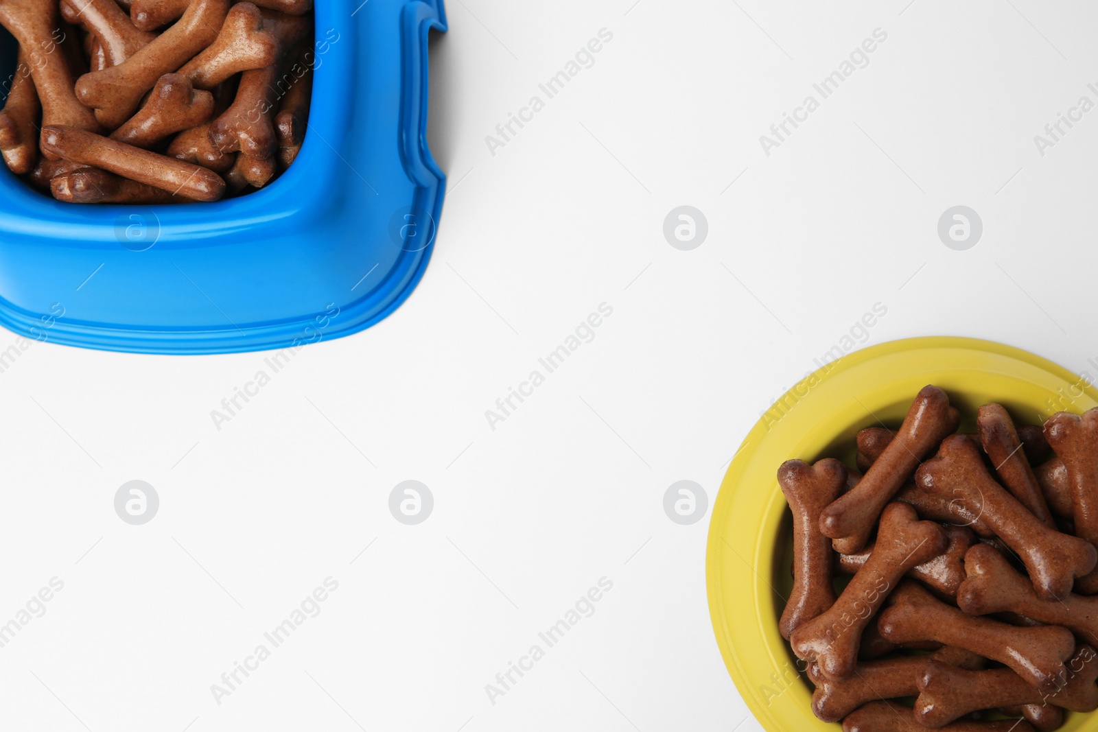 Photo of Bowls with bone shaped dog cookies on white background, top view. Space for text